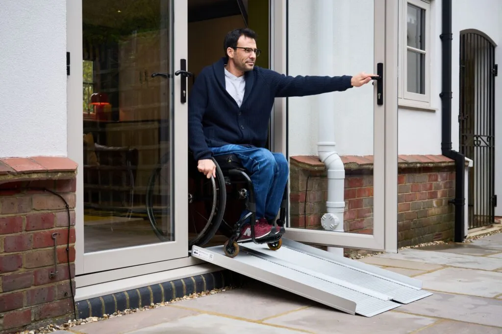 Man in a wheelchair using a Metro folding ramp to access a home