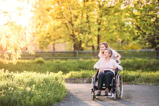 Woman pushing an older lady in a wheelchair on an outdoor path